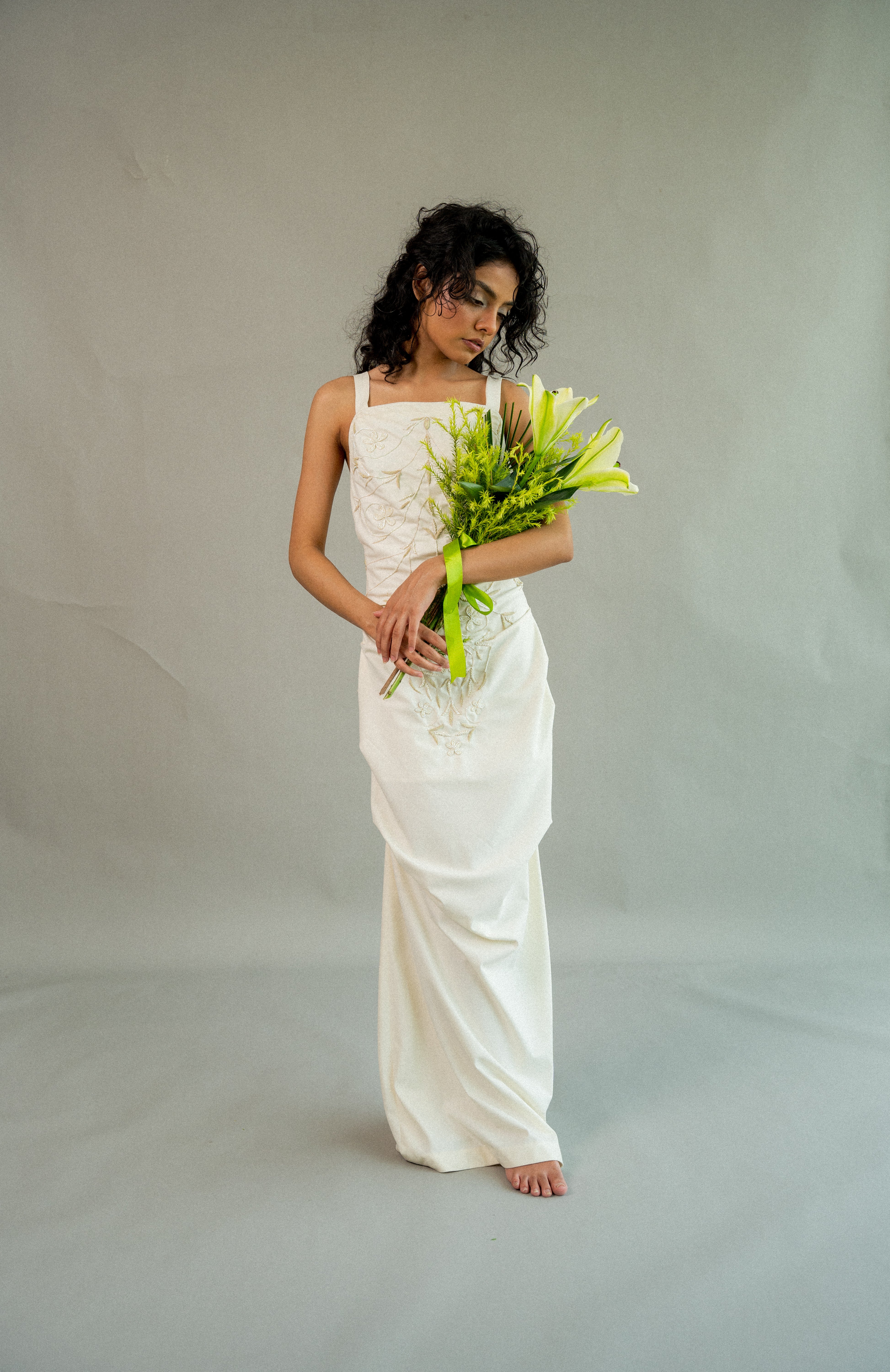 Woman in a white dress holding a bouquet of flowers against a plain background