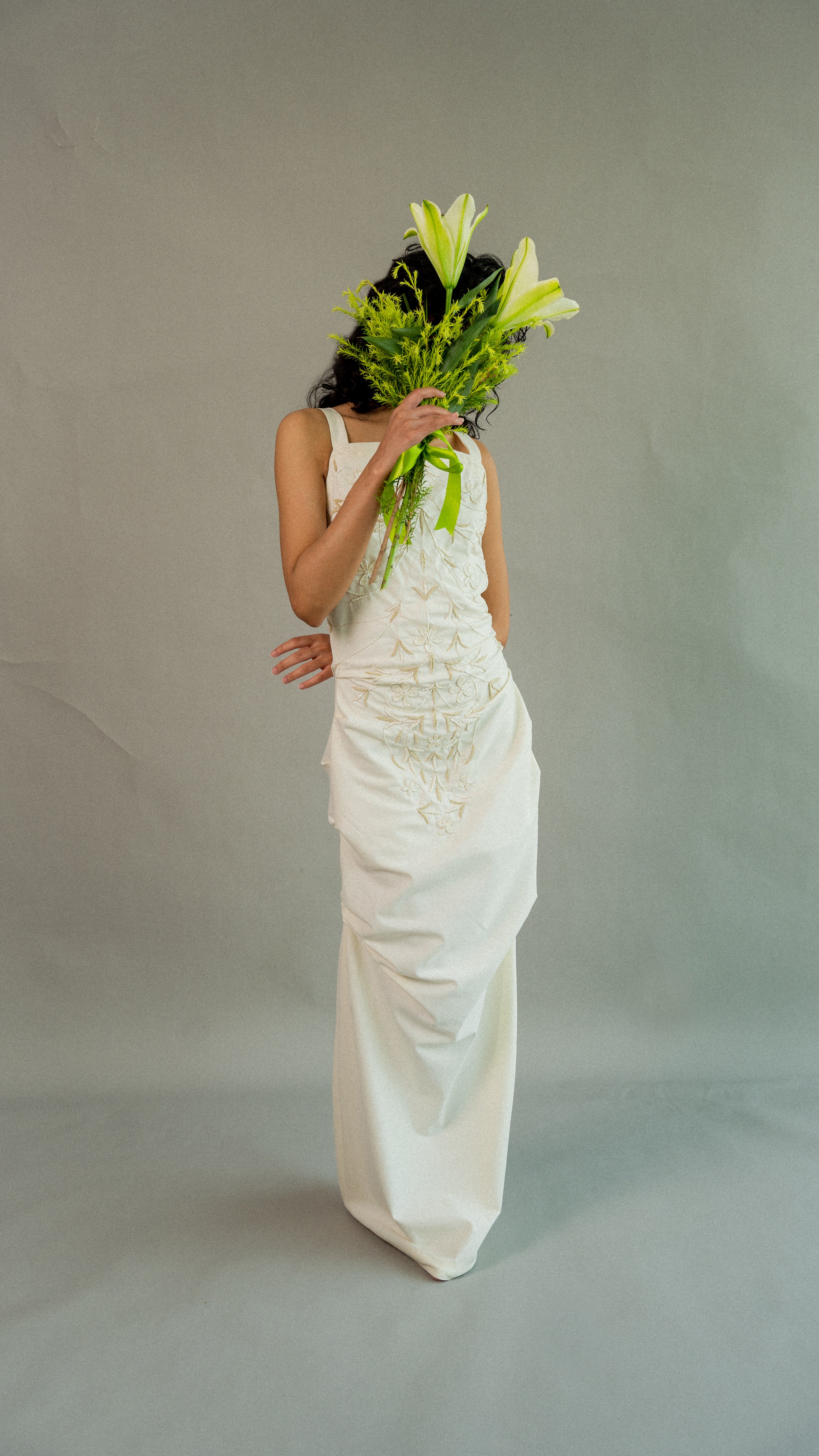 Person in a white dress holding a bouquet of flowers against a plain background