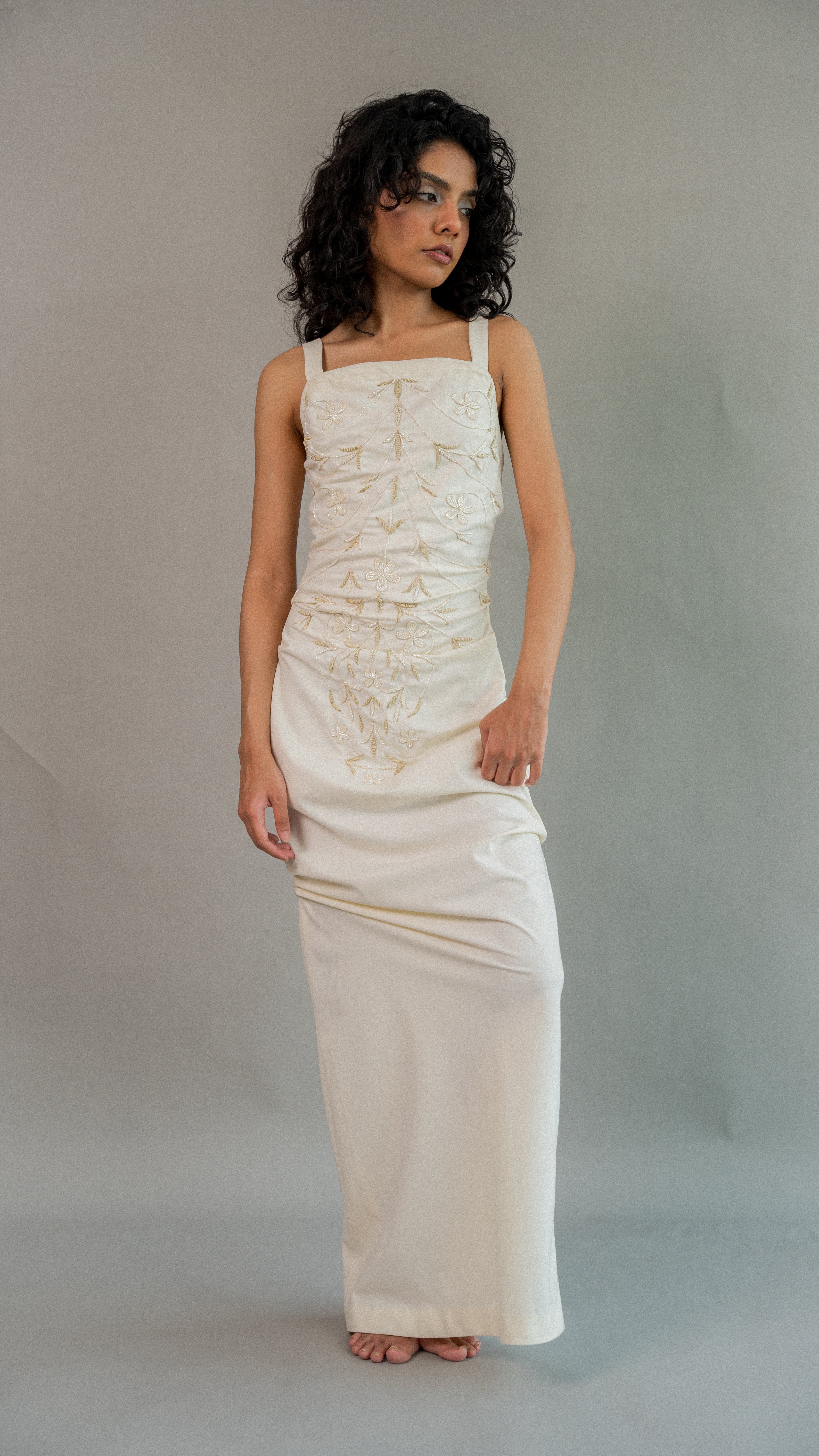 Woman wearing a long, light-colored dress against a plain background