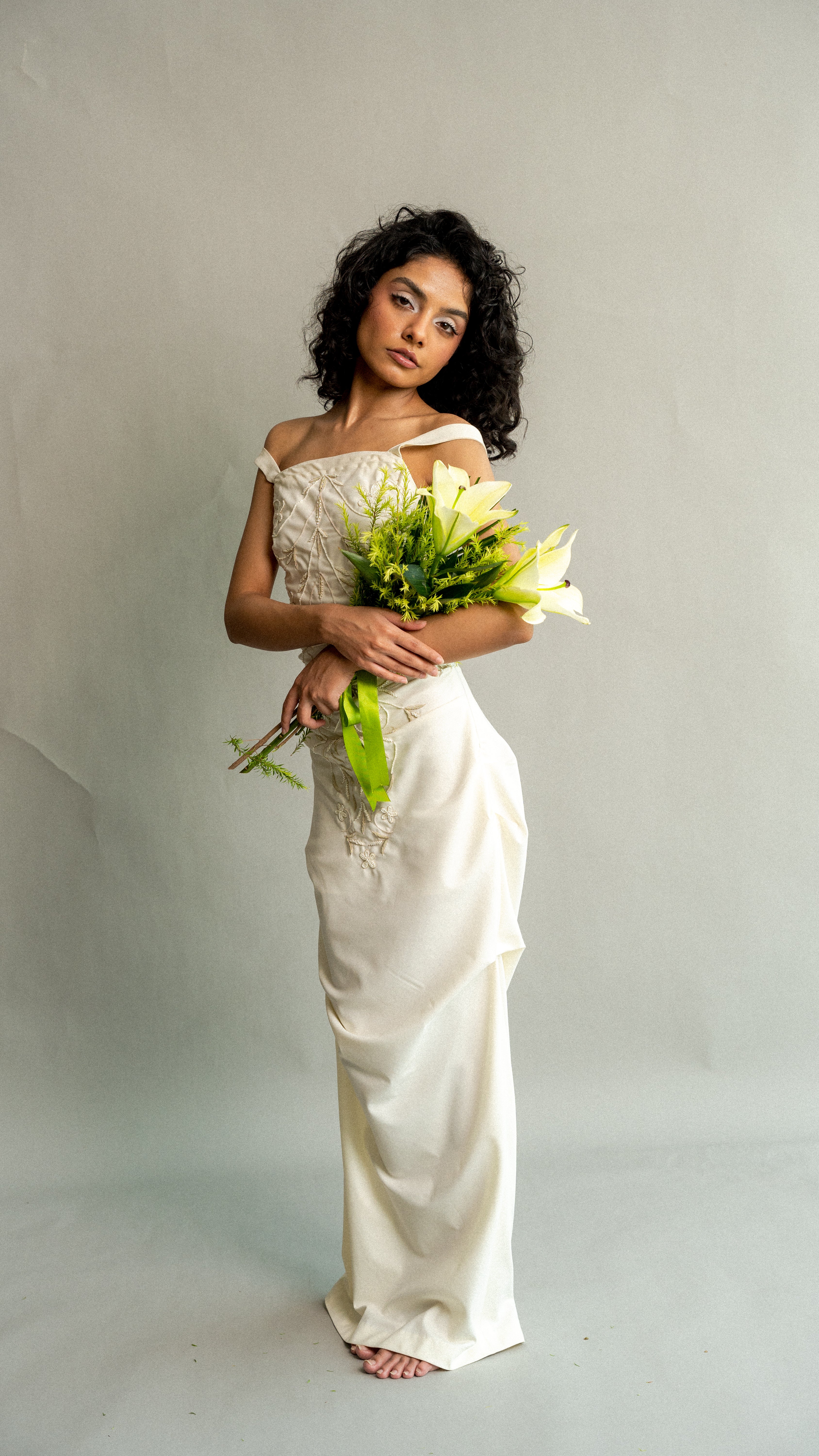 Woman in a white wedding dress holding a bouquet against a plain background