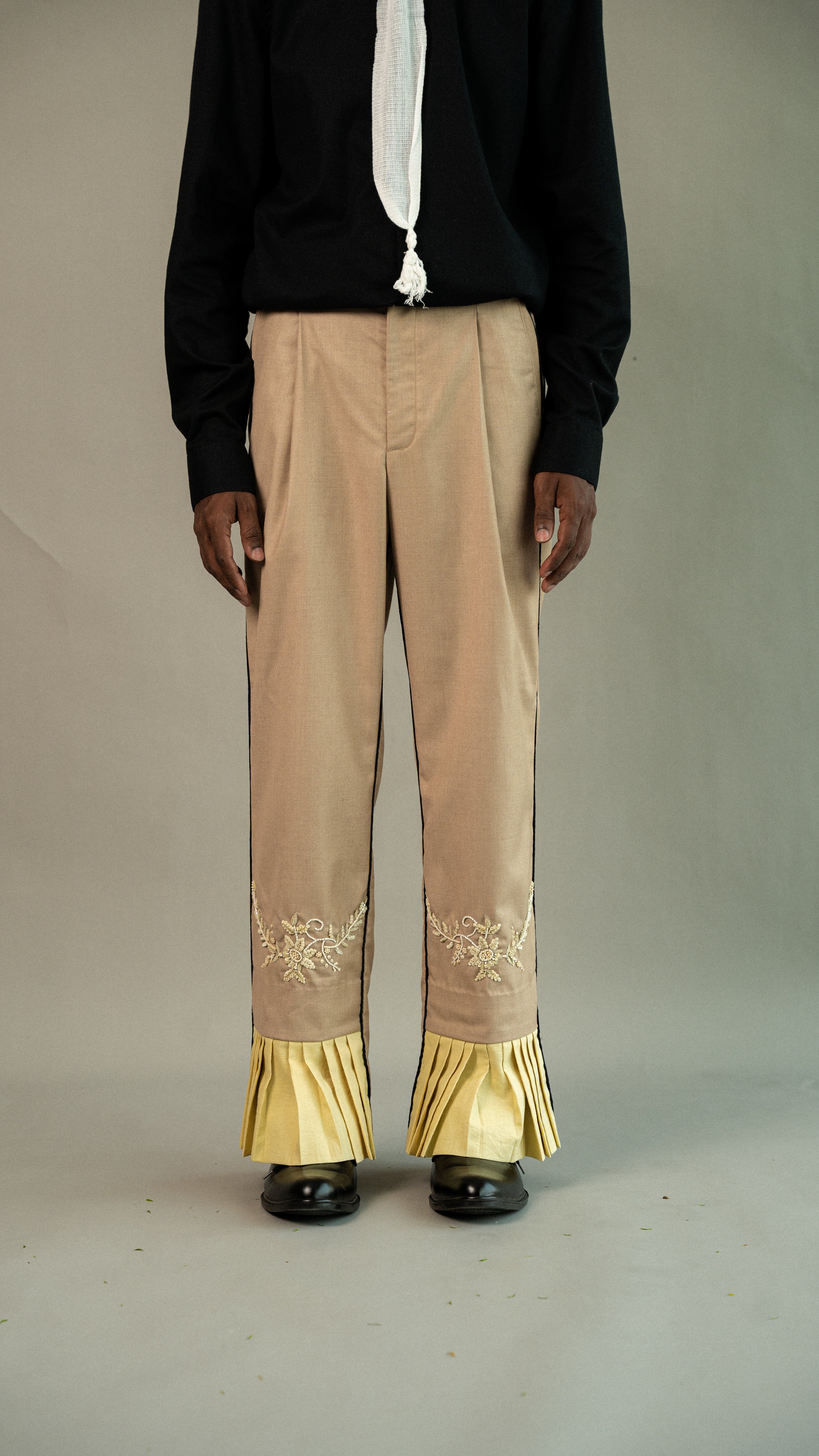 Beige pants with gold trim worn by a person on a plain background