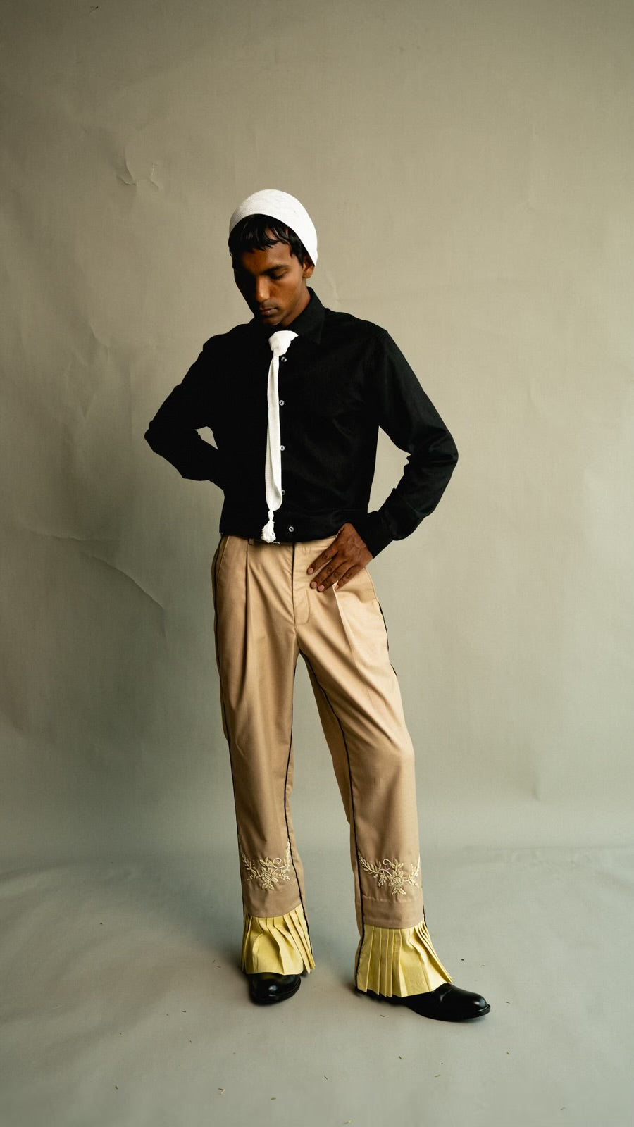 Person wearing a black outfit with beige pants and yellow accents on a plain background