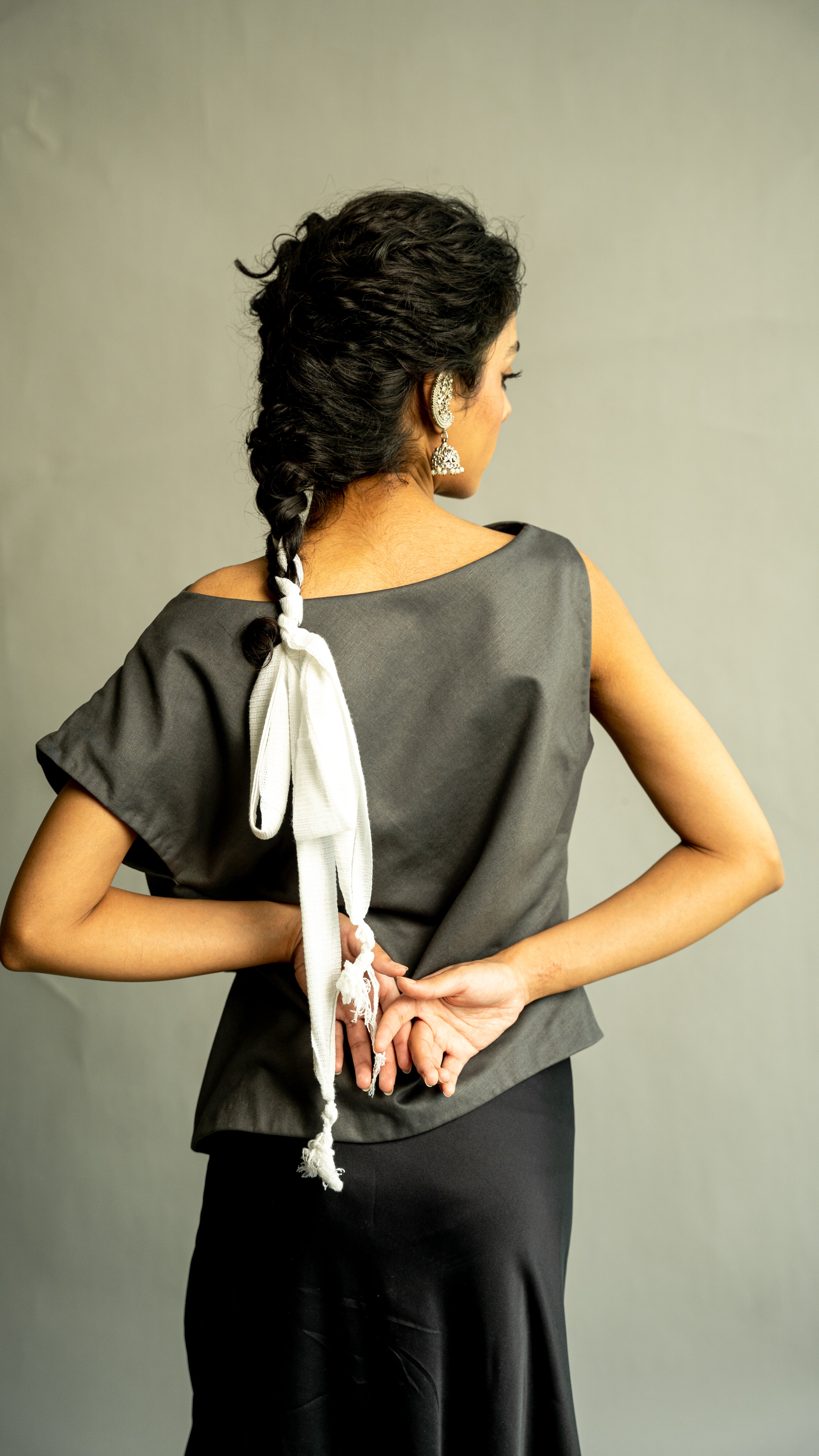 Woman wearing a gray top with a white ribbon and black pants against a plain background
