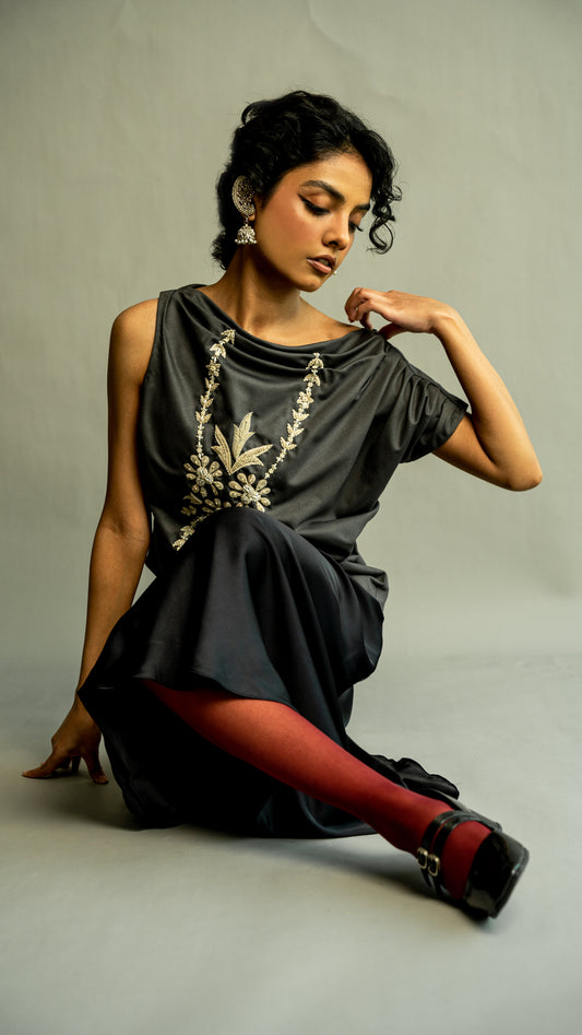 Woman wearing a dark gray dress with gold embroidery on a gray background