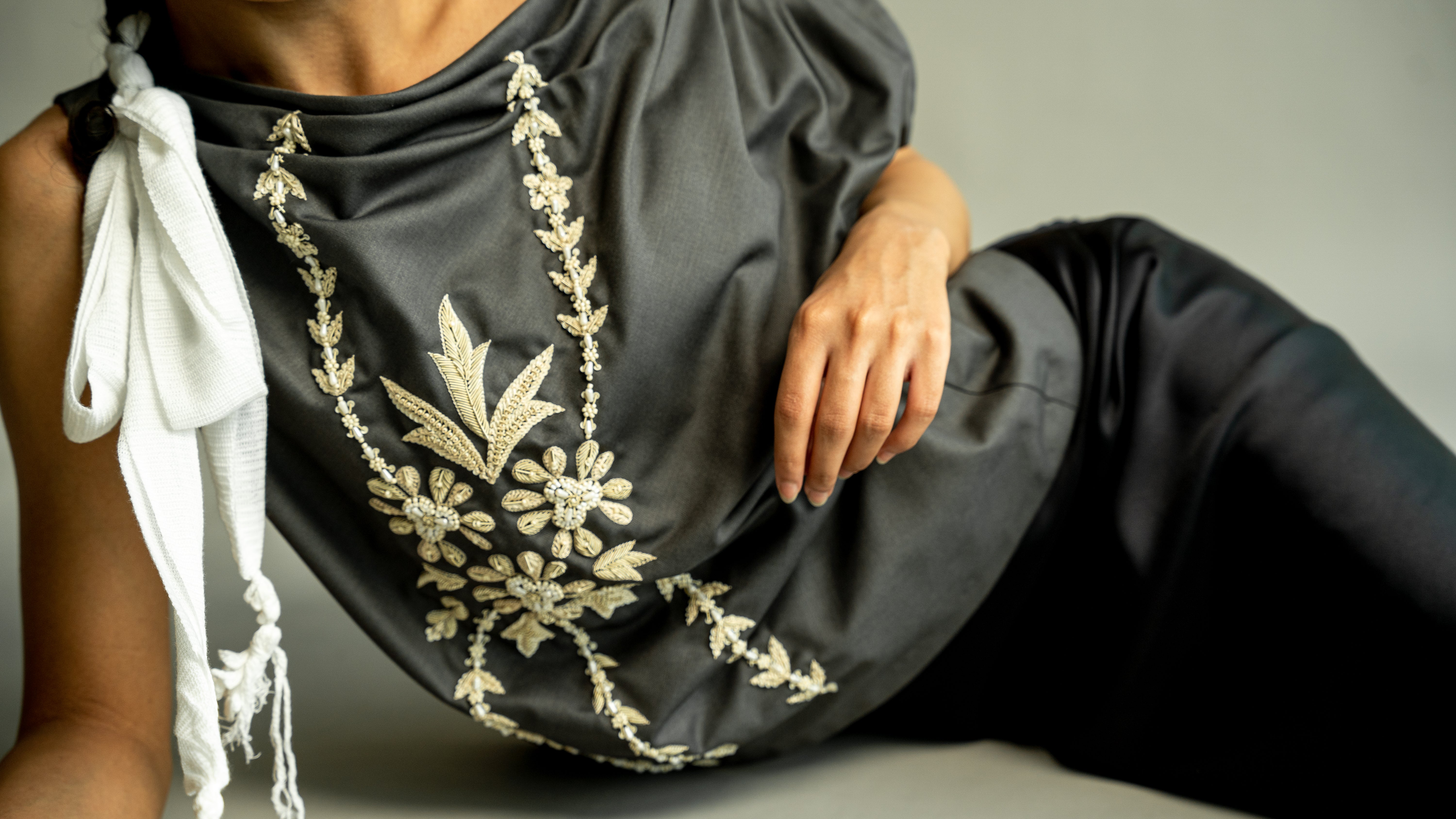 Person wearing a dark gray outfit with white embroidery on a neutral background