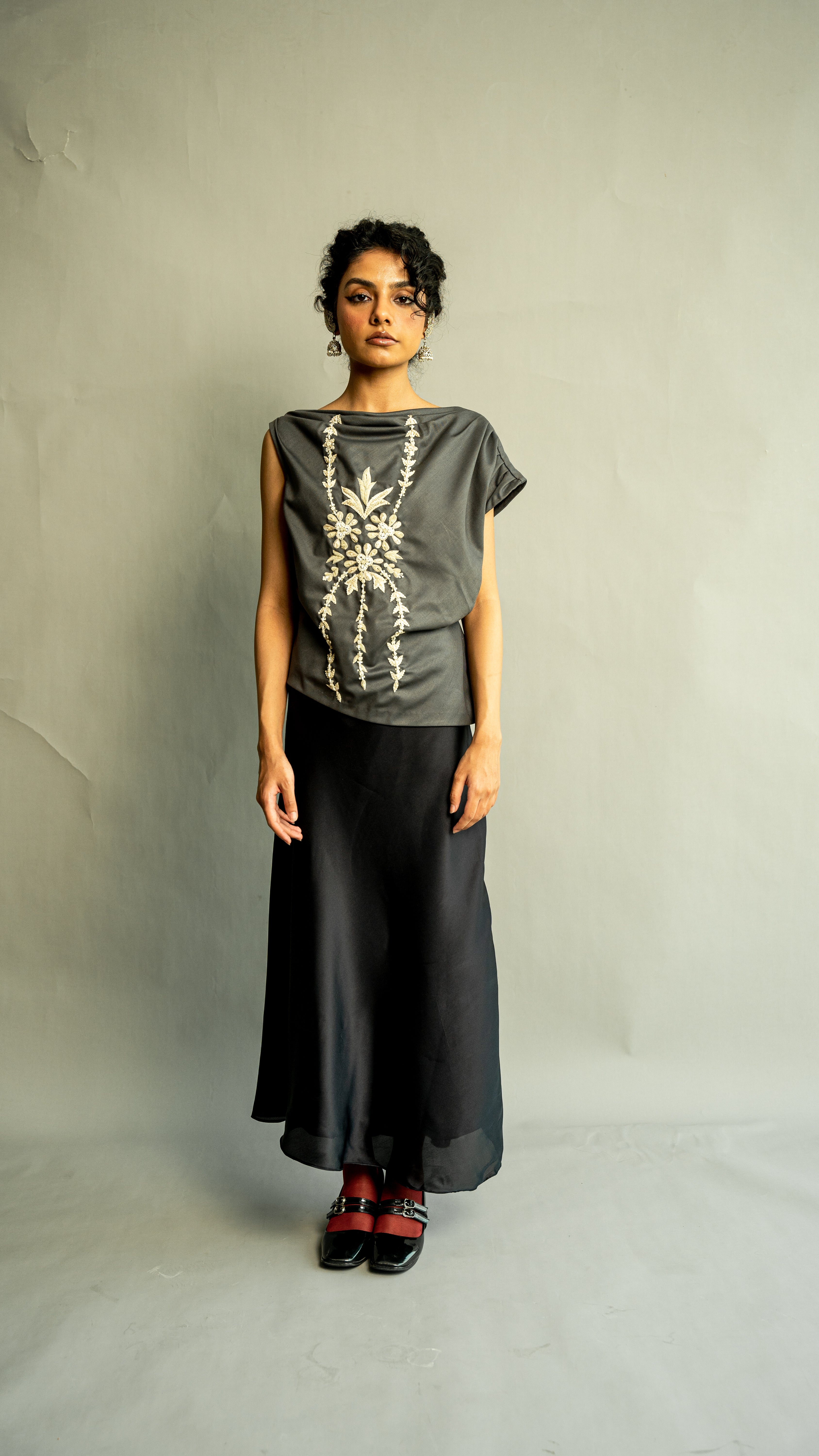 Woman wearing a dark gray top with floral embroidery and black pants on a plain background