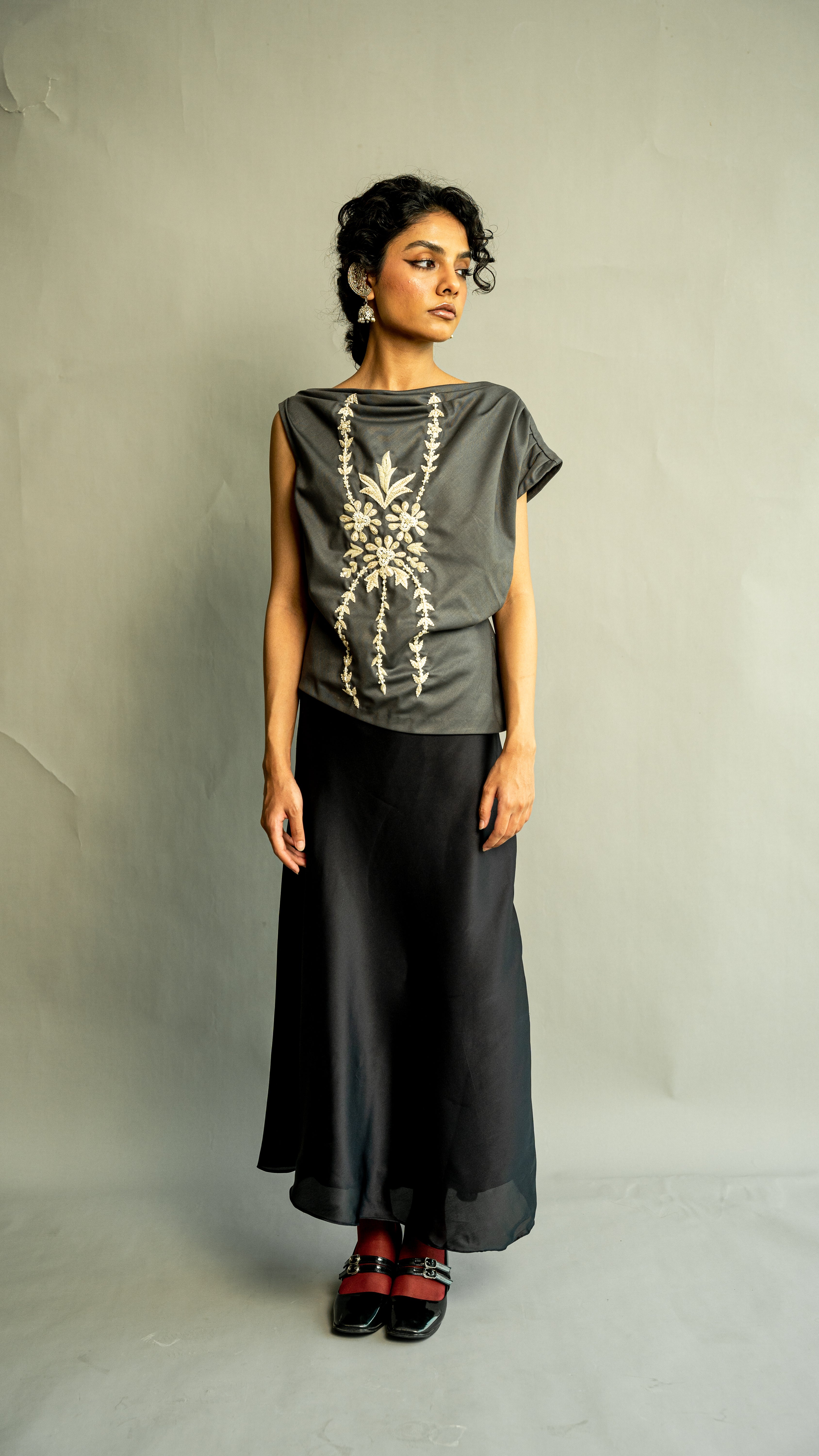 Woman wearing a dark gray top with floral embroidery and black pants against a plain background