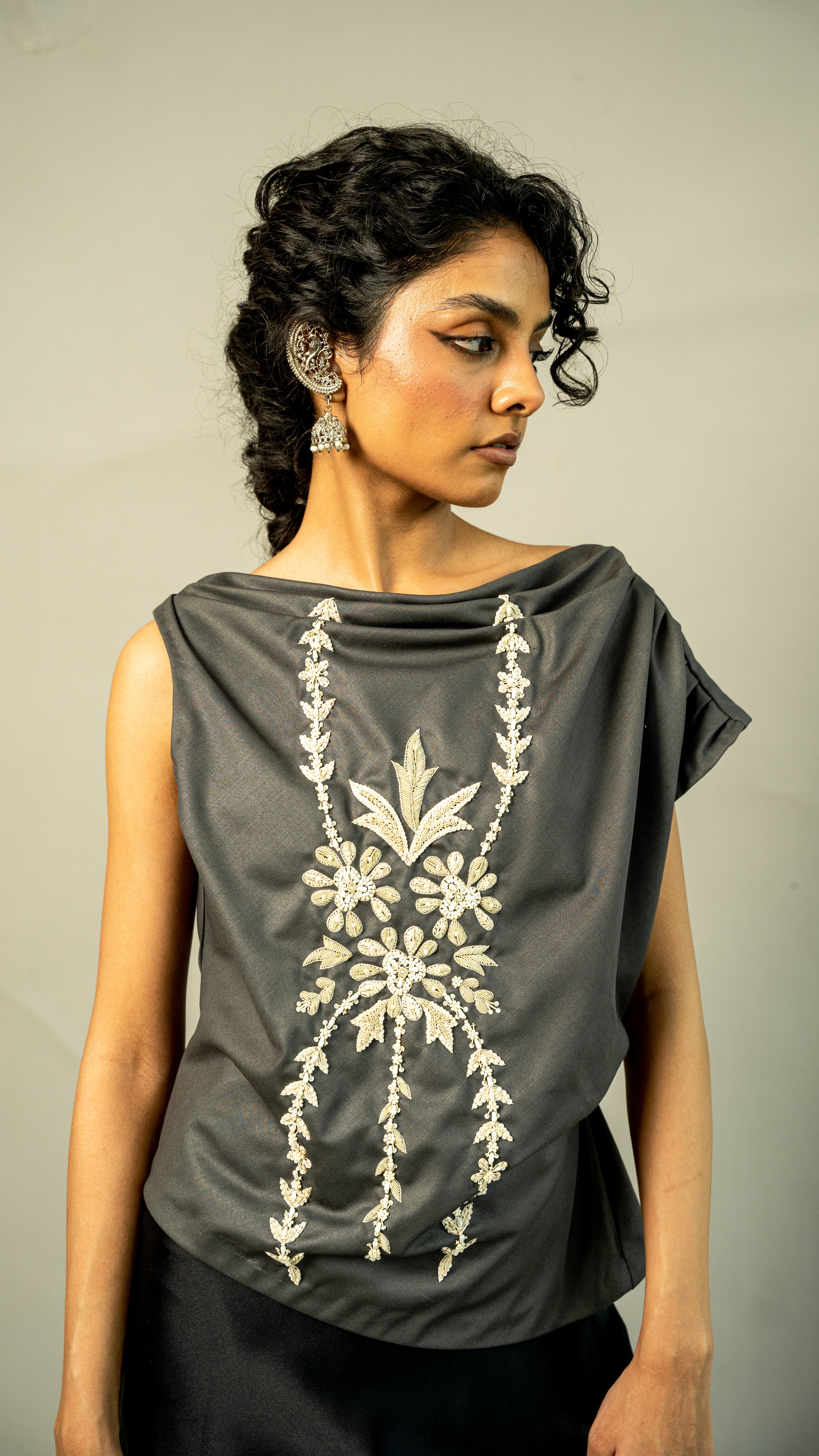 Woman wearing a gray top with white floral embroidery against a neutral background