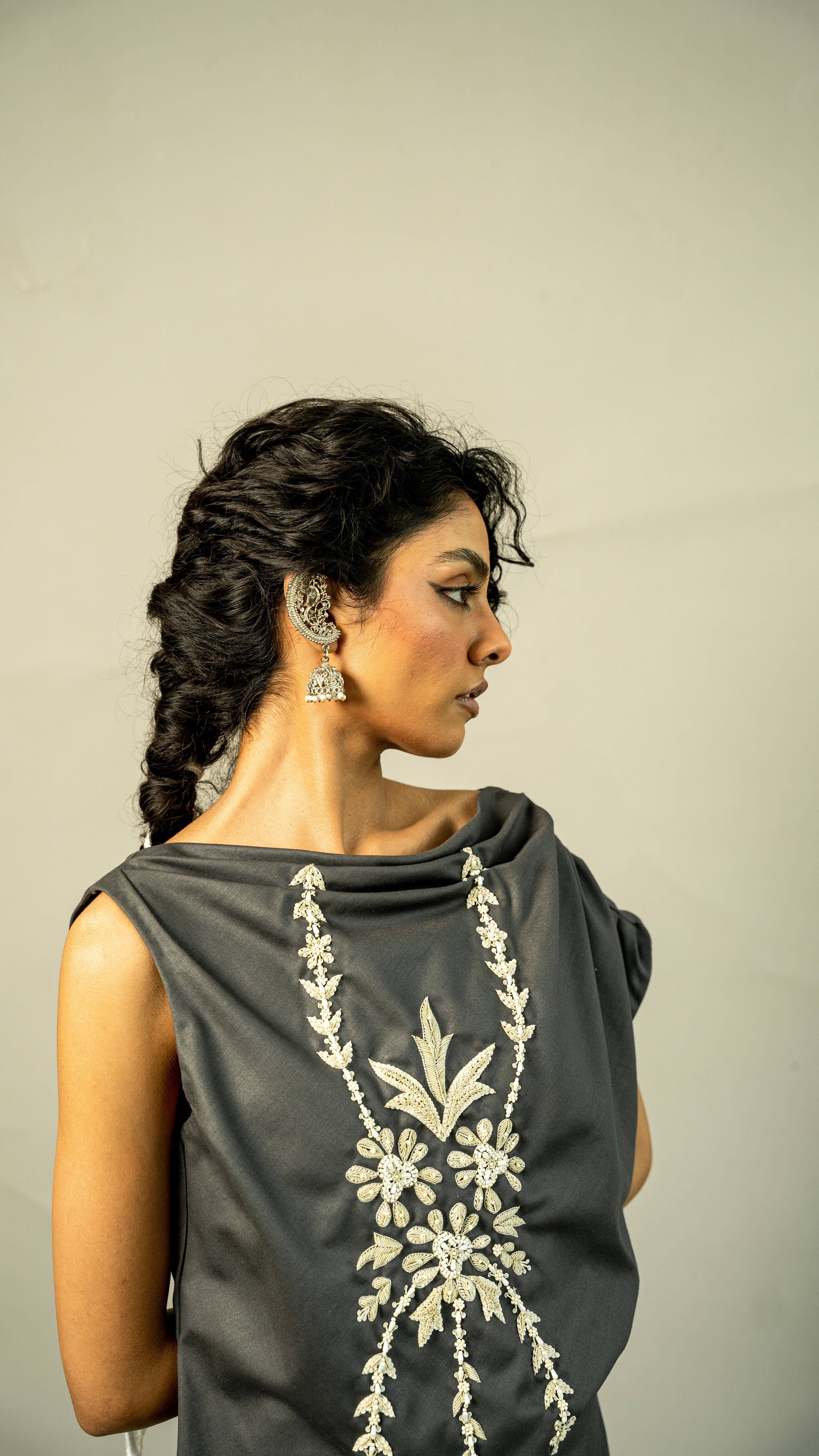 Woman wearing a dark gray dress with white floral embroidery on a plain background