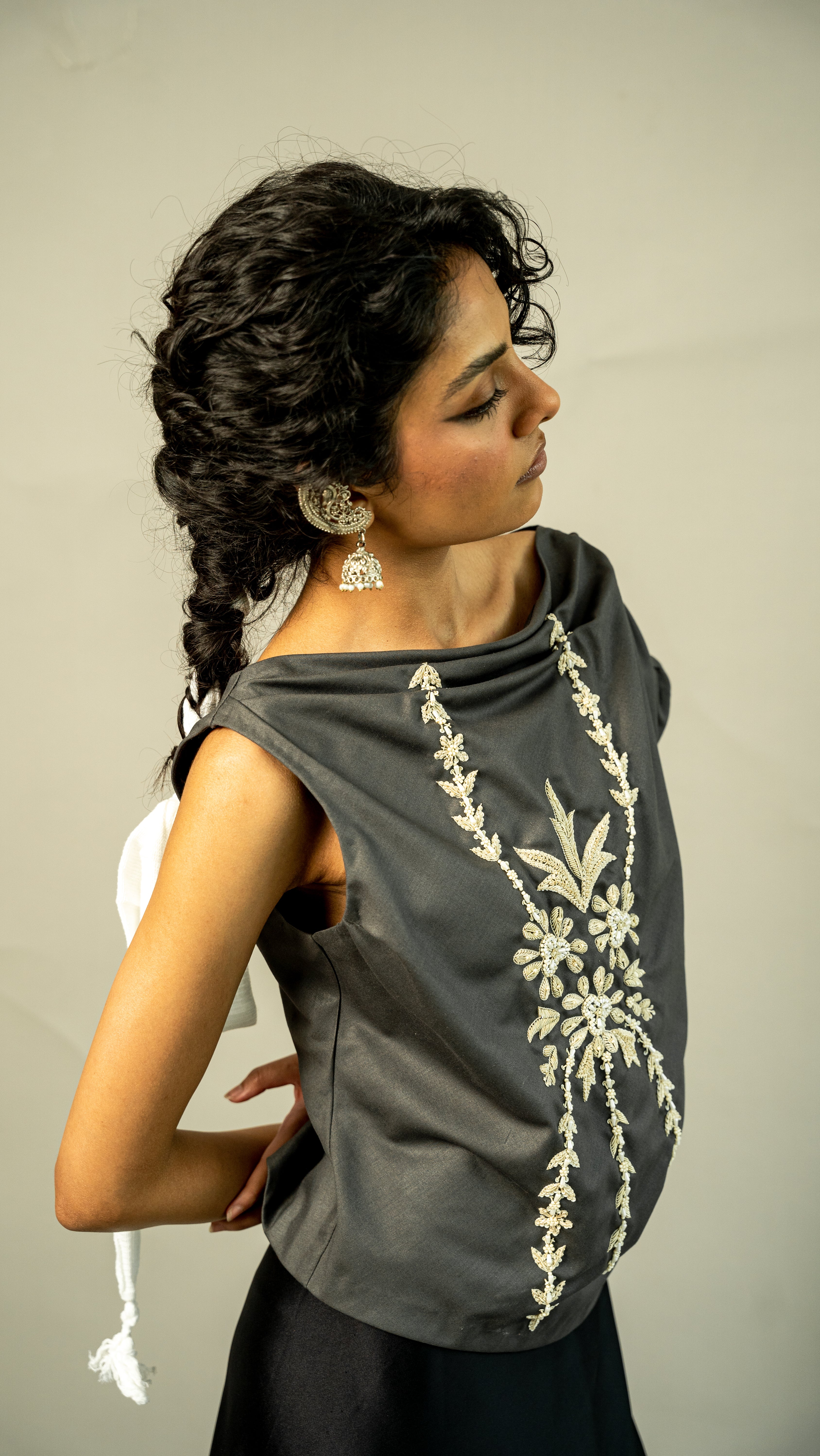 Woman wearing a gray sleeveless top with white floral embroidery against a plain background