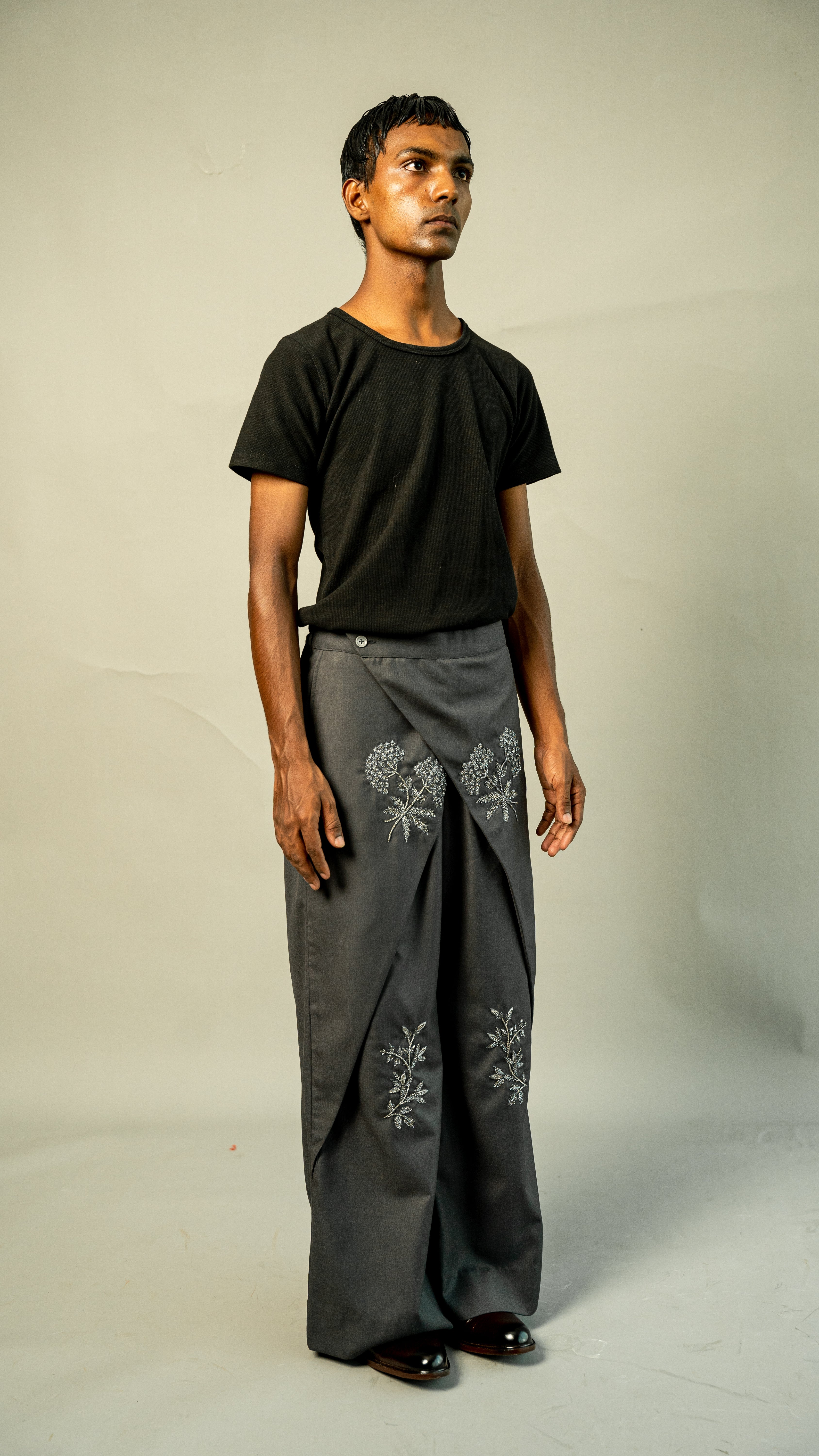 Man wearing a black t-shirt and gray pants with floral embroidery on a plain background
