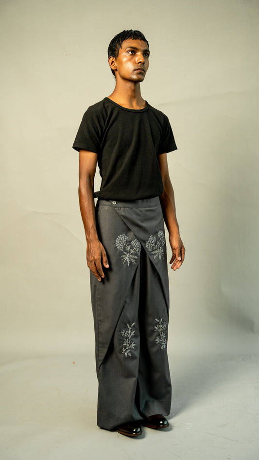 Man wearing a black t-shirt and gray pants with floral embroidery on a plain background