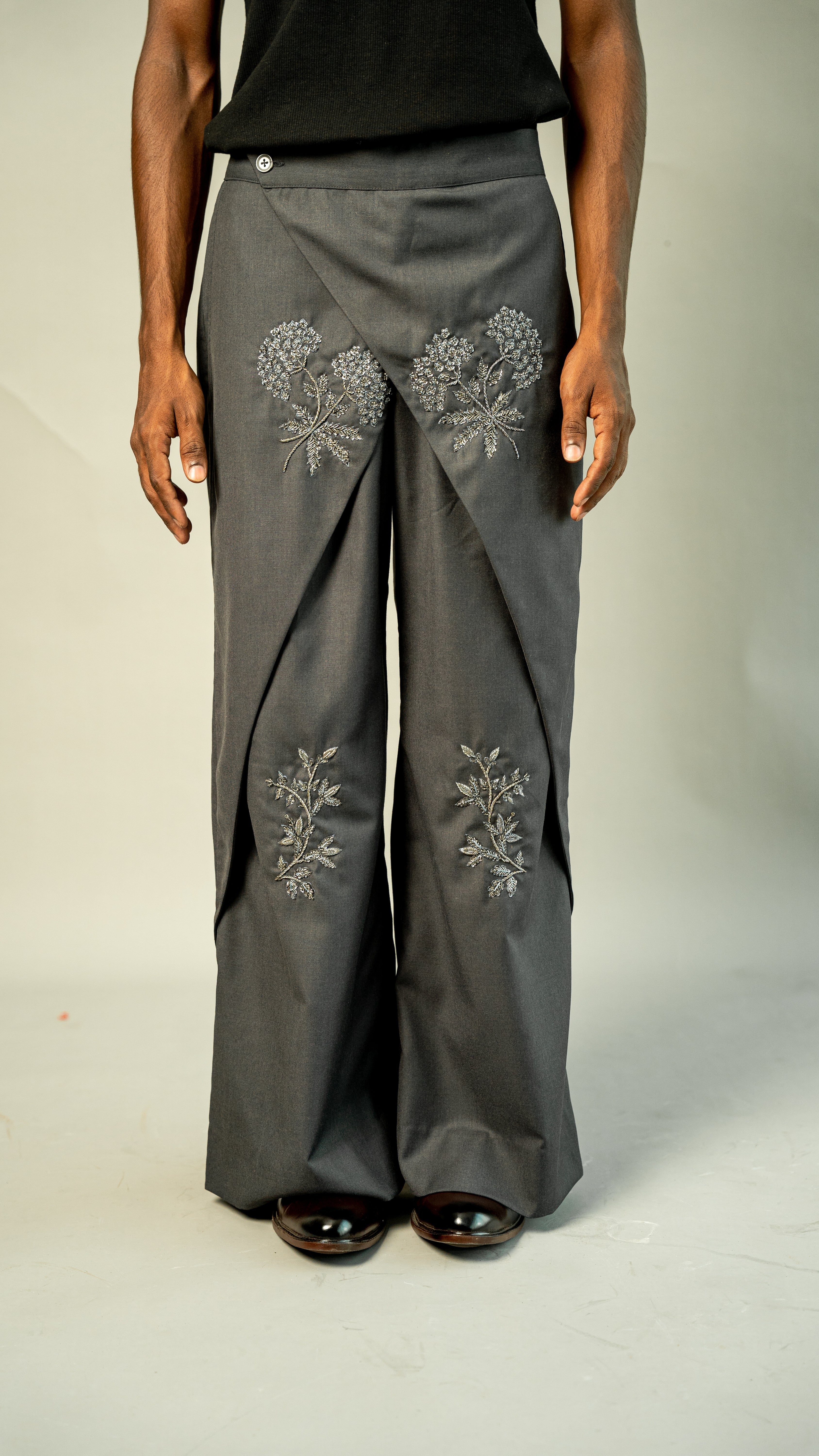 Gray pants with floral embroidery worn by a person on a plain background