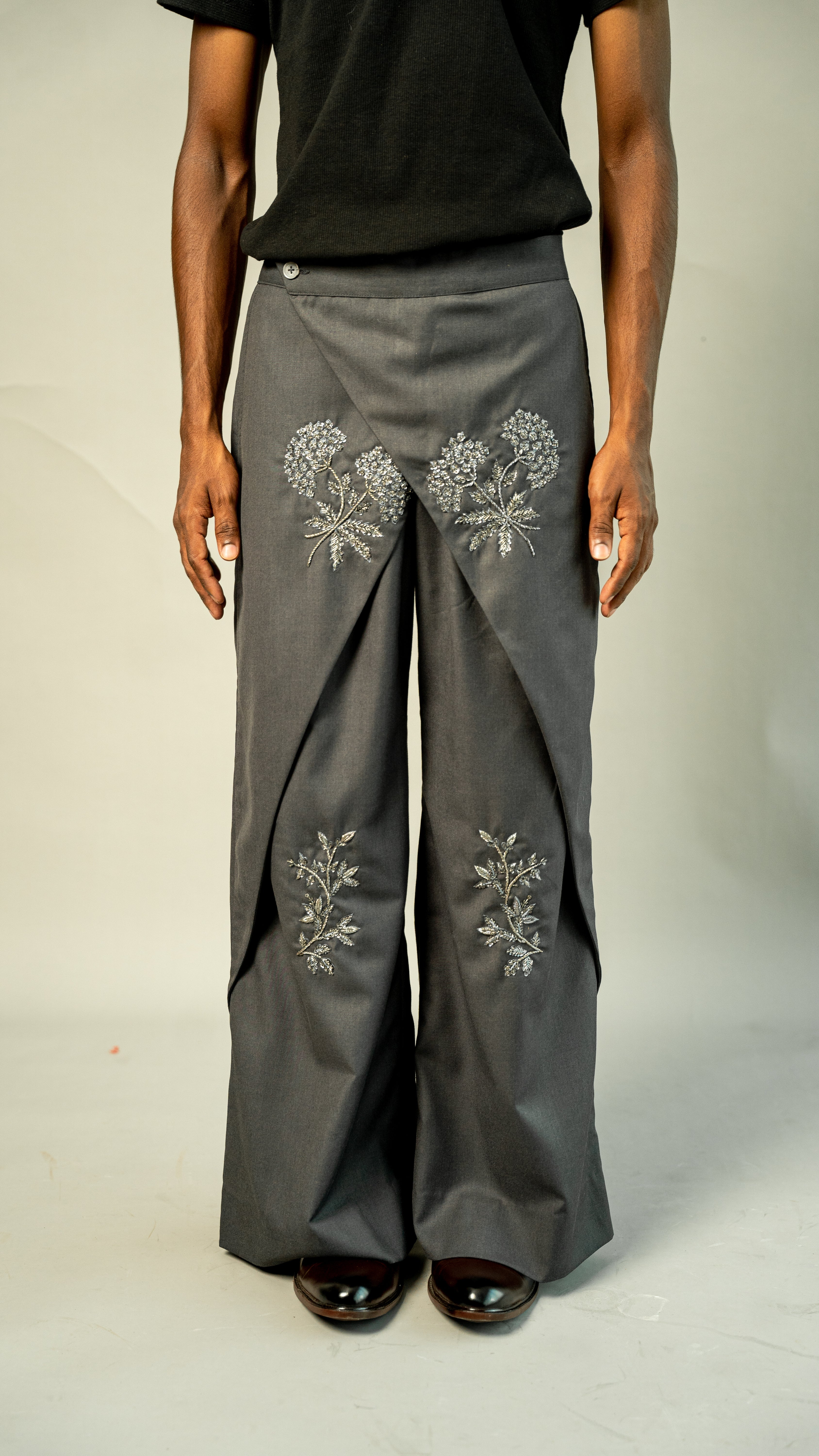 Person wearing gray pants with floral embroidery on a plain background
